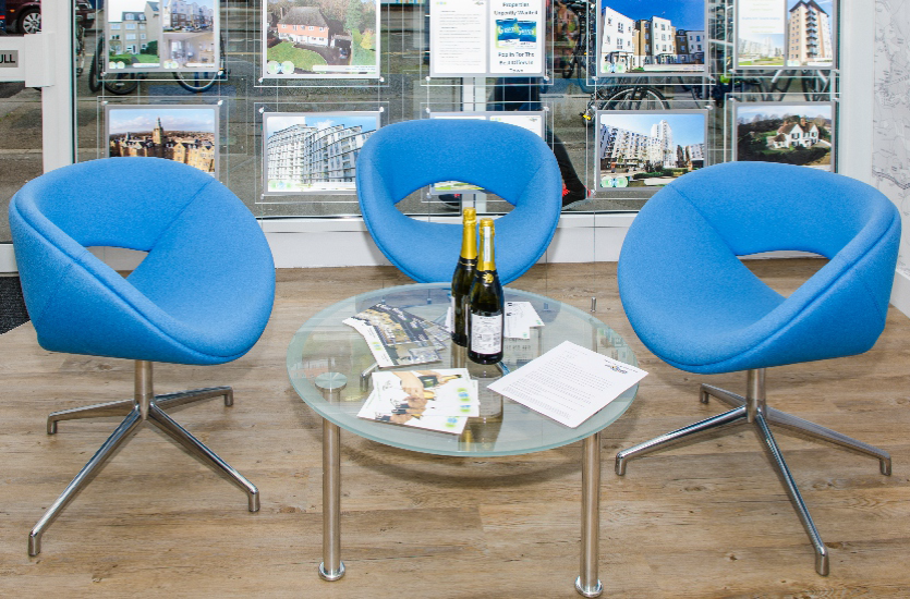 3 blue chairs around a little glass table with bottle on it 