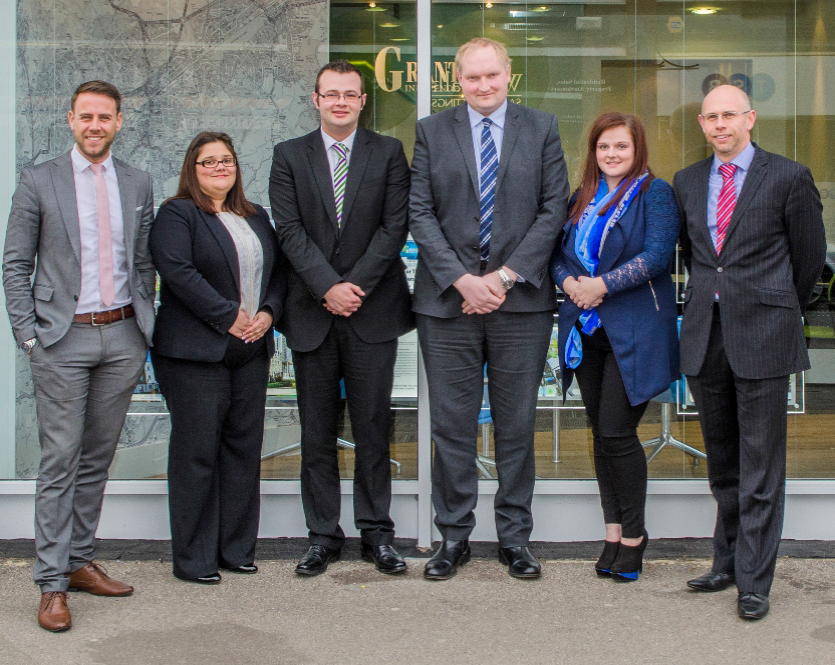 six people standing in a line outside a building in suits 